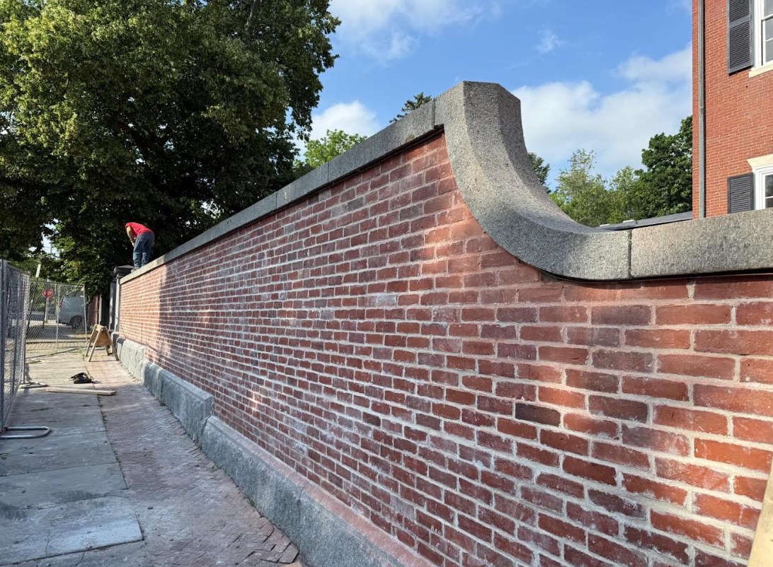 Worker on top of a restored brick wall with a curved granite cap