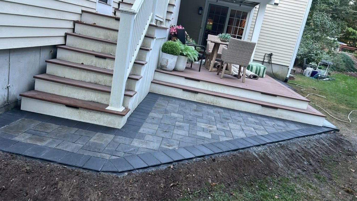 New paver patio with a dark border below a deck and stairs