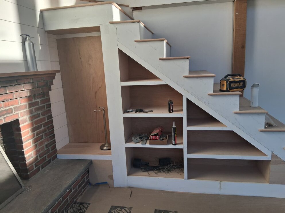Custom white staircase with built-in open shelving underneath, next to a brick fireplace